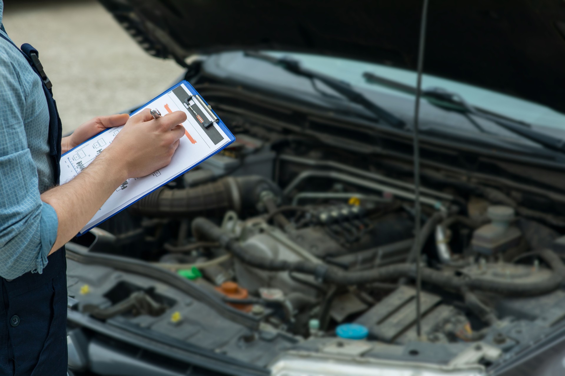 Man writing car checklist while working in auto repair shop.